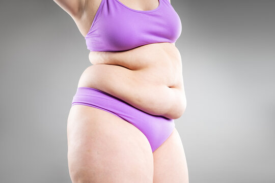 Overweight woman with belly fat in underwear on gray background. Obesity, weight loss, diet and body positivity concept