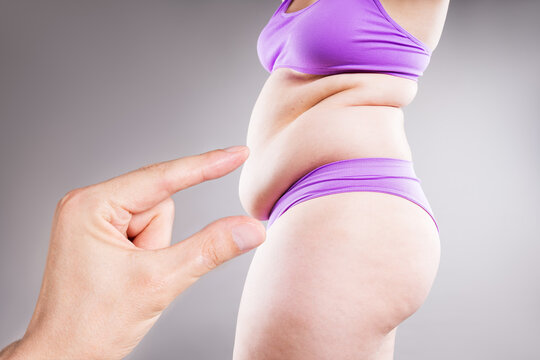 Male hand pointing at belly fat of an overweight plus size woman. Obesity, weight loss, liposuction and body shaming concept