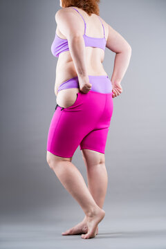 Overweight plus size woman struggling to pull up tight pink neoprene slimming shorts. Weight loss, shapewear and body shaping concept