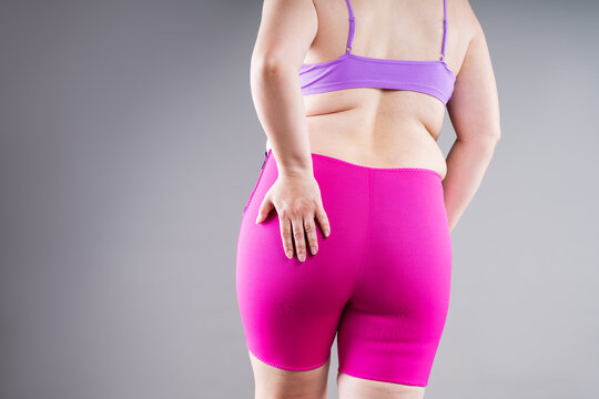 Overweight plus size woman struggling to pull up tight pink neoprene slimming shorts. Weight loss, shapewear and body shaping concept