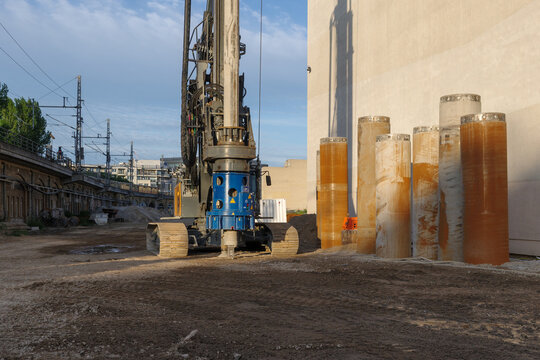 Heavy piling machine boring deep foundations on a city building site with industrial casing pipes and soil