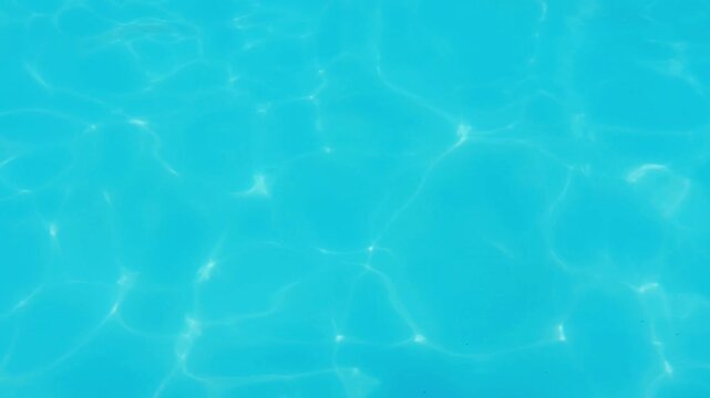 Clear turquoise water surface of a swimming pool with sunlight reflecting, creating a relaxing, calming, and shimmering natural caustic light refraction pattern on the pool floor