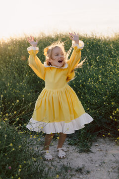 Happy little girl dancing in yellow dress surrounded by wildflowers outdoors