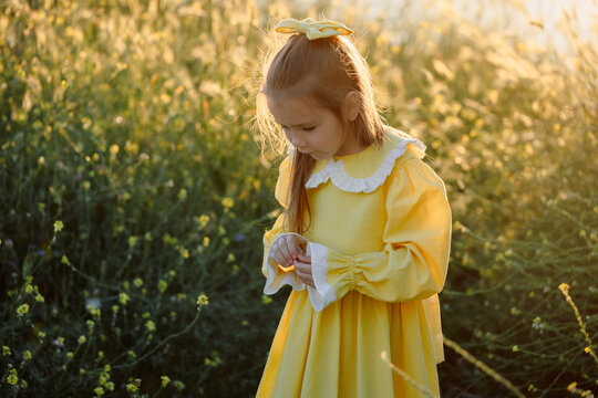 Little elegant girl in yellow dress among flowers enjoying peaceful summer nature