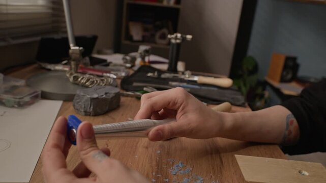 Close up of Caucasian young adult female jeweler sliding blue wax ring mold onto mandrel sizing tool at workbench, tilt up camera motion. For promoting handmade jewelry brands, artisan craft workshops