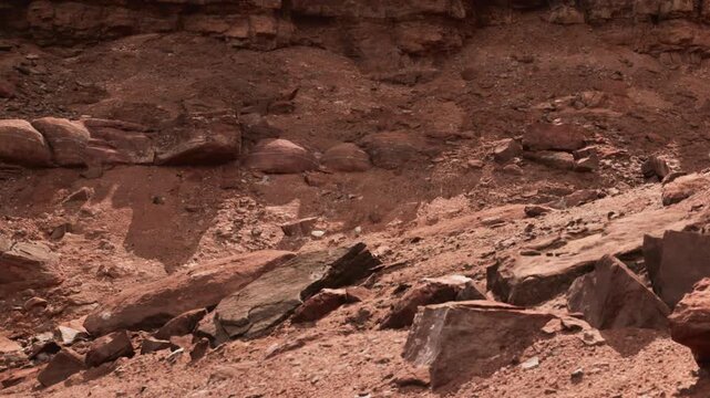 The scene shows a dry area with red and brown rocks scattered across the ground. The terrain is uneven and dusty, suggesting a remote and barren environment.