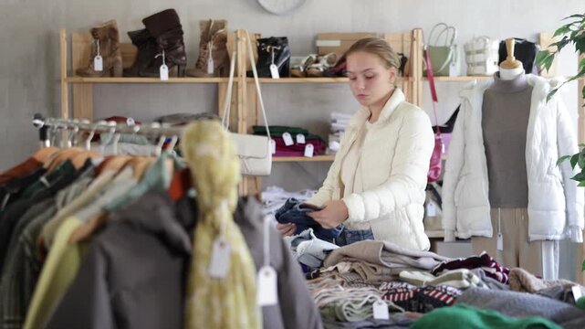 Attentive teenage girl looking for jeans pantaloons for cold season during sell-out in retail outlet