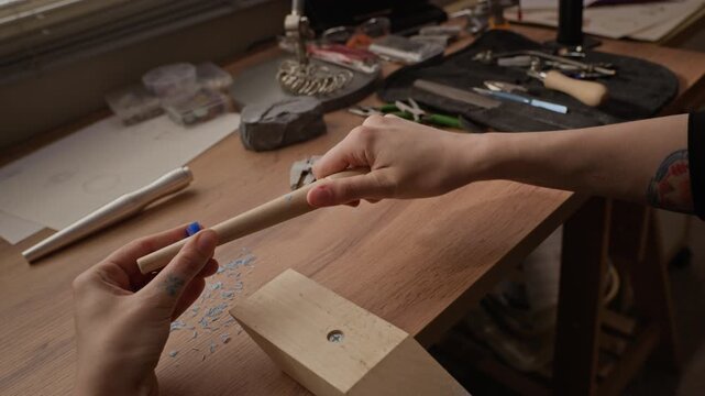 Close up dolly away shot of Caucasian young adult female jeweler using wooden ring mandrel to measure blue wax ring model at workshop bench. For promoting handmade jewelry brands and craft workshops