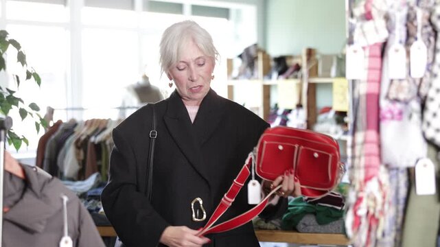 Older woman choosing a stylish bag, paying attention to convenience and functionality. She is looking for a handbag that will complement everyday look. Buying clothes and accessories in a boutique 