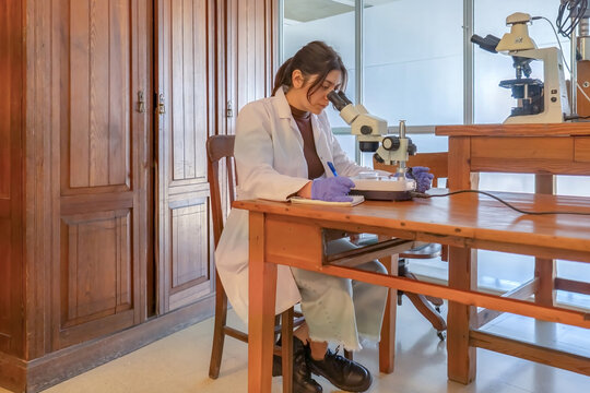 Female scientist using microscope and taking notes in laboratory