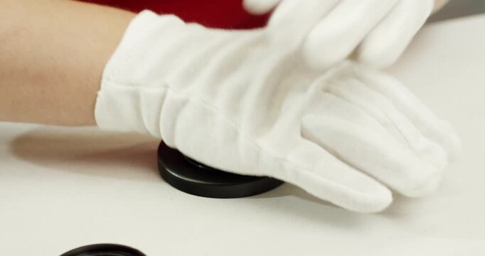 Worker wearing white gloves assembling black circular plastic components on a clean white surface