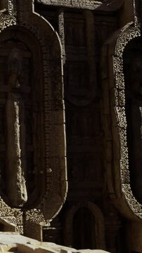 Ancient stone carvings at a temple in India show detailed designs and figures. Light from the sun falls on the carvings, highlighting their craftsmanship and age. Visitors explore the site.
