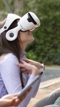 Vertical video: Fixing VR headset woman in top looking up smiling at park seat as hand tapping cell