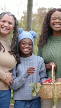 Vertical video: Smiling family in garden as camera zooming, child picking red pepper from basket