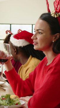 Vertical video: Raising lady in red knit with reindeer headband talking for toast at home with wine