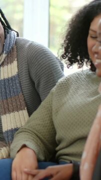 Vertical video: Laughing friends on couch meeting eyes, panning right to woman in leather smiling