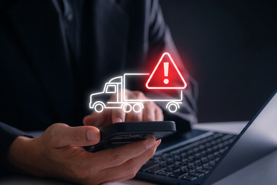 Hand Holding Smartphone with Warning Truck Symbols on Digital Screen Over Dark Keyboard Background