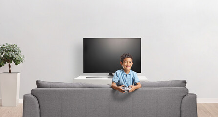 Boy holding a gamepad and sitting behind a sofa © Ljupco Smokovski