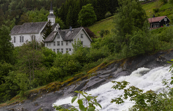 Historic white wooden church and house beside rushing waterfall in Norwegian village