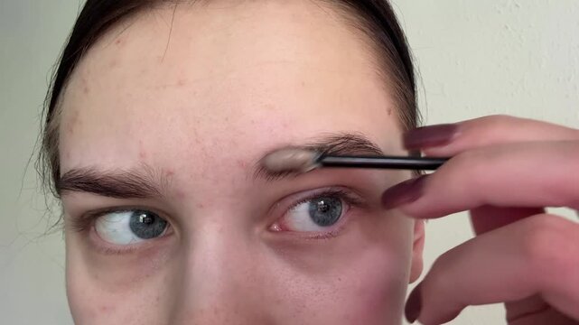 Woman applying eyebrow gel to brow, utilizing brush applicator for precise tinting, performing cosmetic beauty routine, facial grooming process, achieving desired glamour appearance.