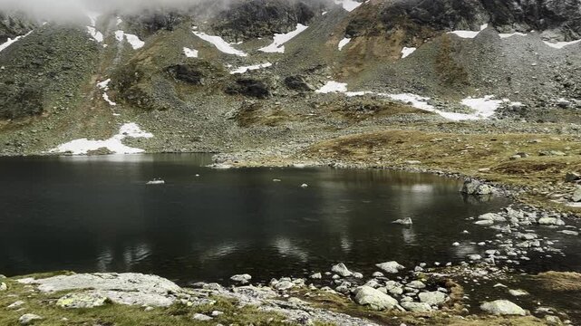 Dramatic Dark Alpine Lake Reflecting Rocky Snowy Slopes in Tatra Mountains Fog. Velke Hincovo pleso 