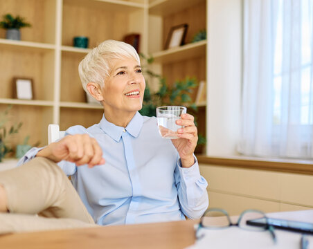 Portrait of a mature senior  businesswoman resting after a meeting and drinking water in the office