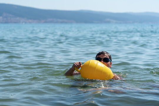 Small boy alone in open water holding onto marker buoy. Concept of swimming beyond beach safety markers, child supervision, water safety awareness and drowning prevention