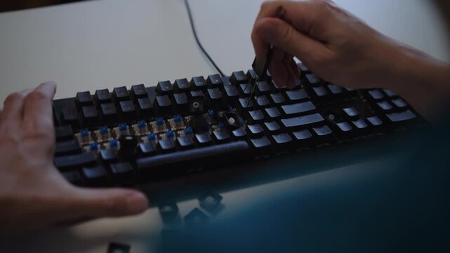 Close-up of specialist hands removing keycaps from mechanical keyboard using special tool for maintenance, repair, cleaning of dusty electronic device on desk. Shooting in slow motion