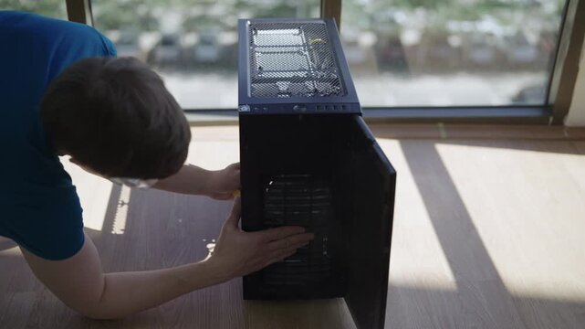 Skilled technician in safety glasses cleaning dust from desktop computer case with can of compressed air, performing regular maintenance and preventing overheating of components, slow motion