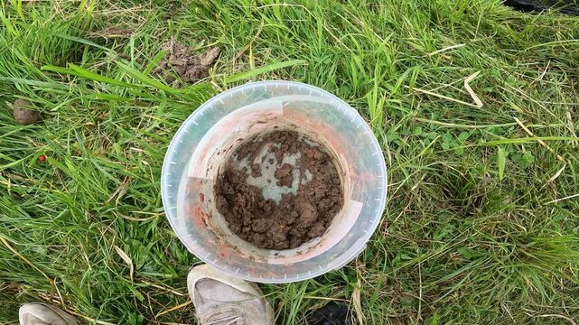 Top down view of fishing bait bucket with mixed groundbait on green grass, carp angling preparation outdoors