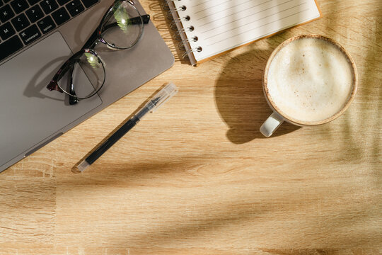 Home office workspace with notebook, coffee and eyeglasses on wooden desk, top view with copy space