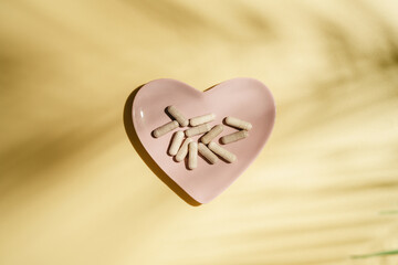 Fototapeta premium Collagen supplement capsules on yellow background with leaf shadows, flat lay and copy space