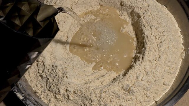 Pouring water into a flour well in a metal bowl, close up