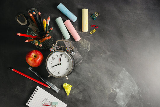 Blackboard workspace with school supplies and alarm clock, education background, back to school concept