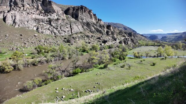 Vardzia, a 12th-century rock-cut cave monastery complex, is carved into Erusheti Mountain in Georgia, overlooking the flowing Mtkvari River amidst green landscapes and a clear blue sky