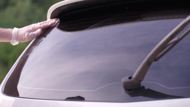 A man applies a ceramic anti-rain coating to the windows and headlights of a car.