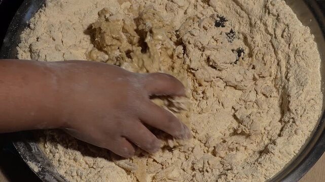 Baker kneading and mixing dough by hand in a metal bowl, top view