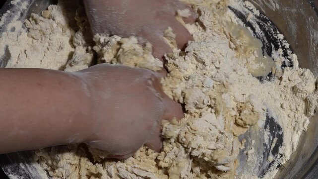 Kneading raw dough by hand in a metal bowl close up, top view