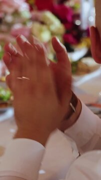 Vertical video. Unrecognizable man clapping hands at wedding reception with blurred floral background.