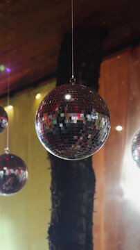 Vertical video. Mirror disco balls spinning from ceiling at wedding reception venue.
