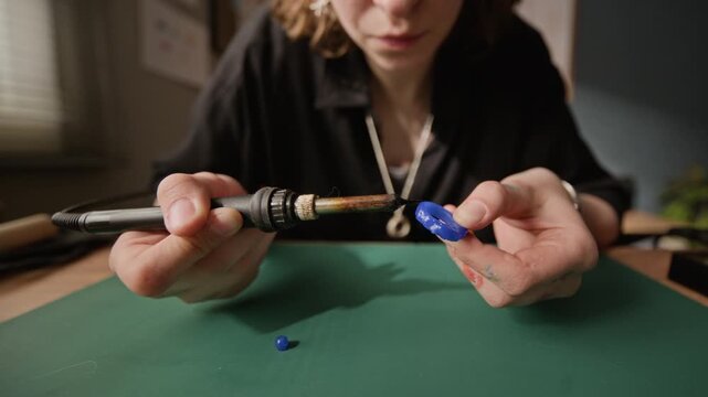Close up of Caucasian young adult female jeweler using soldering iron to shape blue wax ring model at workshop. Footage perfect for promoting handmade jewelry brands or artisanal craft courses