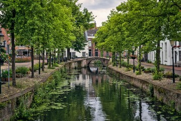 Fototapeta premium Picturesque Historic Canal with Stone Arch Bridge and Green Trees in Amersfoort