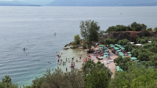 Garda Lake, Bardolino, Italy. Lake beach with clear green waters and people sunbathing during summer day.