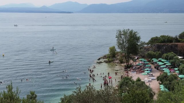 Garda Lake, Bardolino, Italy. Lake beach with clear green waters and people sunbathing during summer day.
