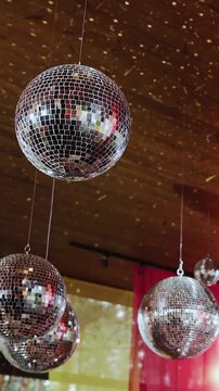 Vertical video. Rotating mirror disco balls suspended from ceiling at wedding venue.