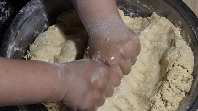 Hands kneading raw bread dough in a large metal bowl, top view