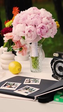 Vertical video. Wedding bouquet of pink peonies on table with vintage camera and Polaroid photos.