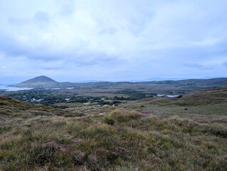 Fototapeta premium Distant hikers walking on a trail through the vast, rugged landscape of Connemara National Park in Ireland.