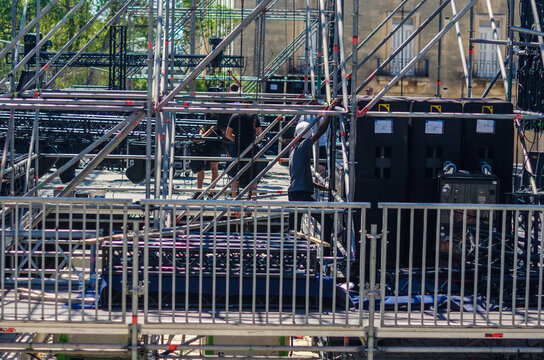 Outdoor concert stage setup backstage area with scaffolding flight cases trucks and crew vehicles preparing for a live event on a sunny day