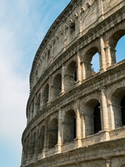 Obraz premium Ancient Roman Colosseum exterior with arched facade and stone columns against blue sky in Rome Italy